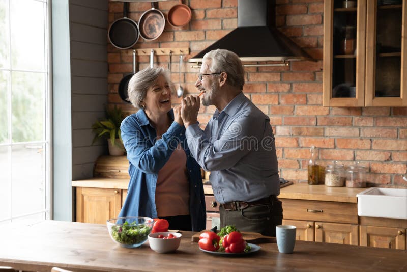 Happy senior husband and wife cooking at home together