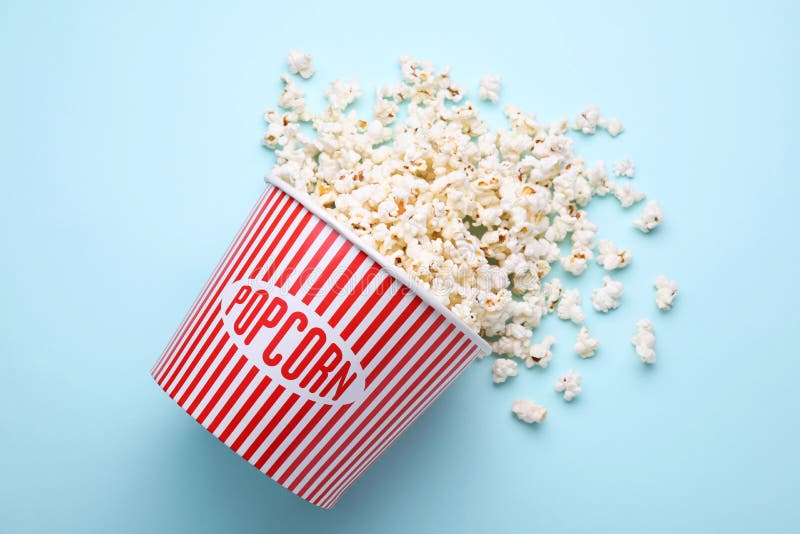 Overturned Paper Bucket with Delicious Popcorn on Light Blue Background