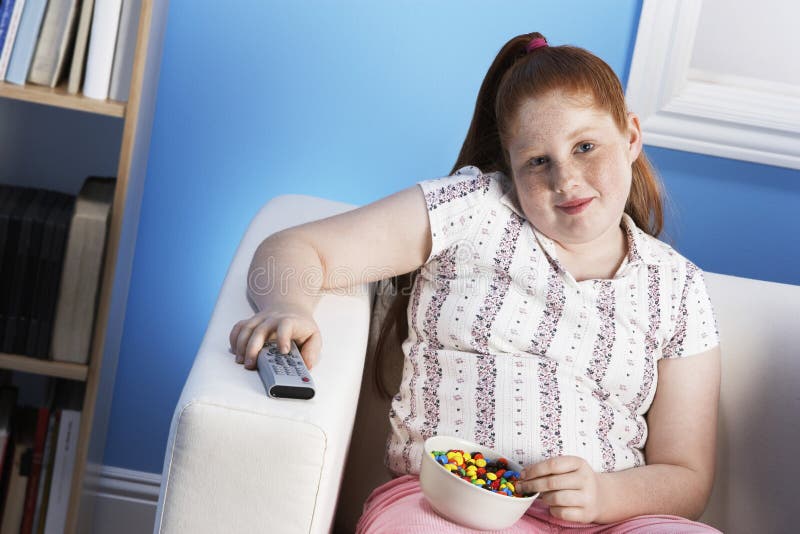 Overweight Girl With Remote Control Eats Junk Food On Couch Stock Image