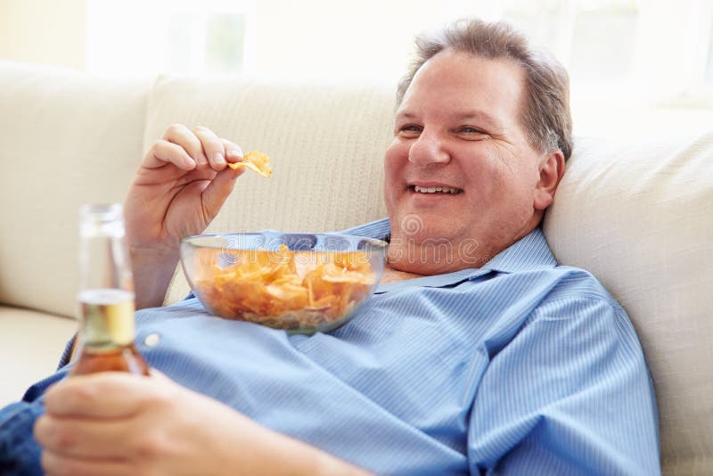 Overweight Man at Home Eating Chips and Drinking Beer Stock Photo