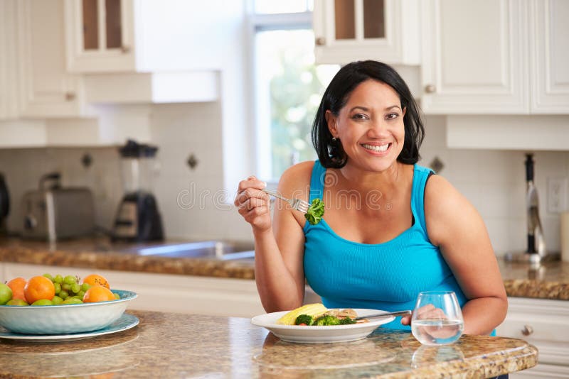 Overweight Woman Eating Healthy Meal in Kitchen stock photo Overweight Woman Eating Healthy Meal in Kitchen stock photo