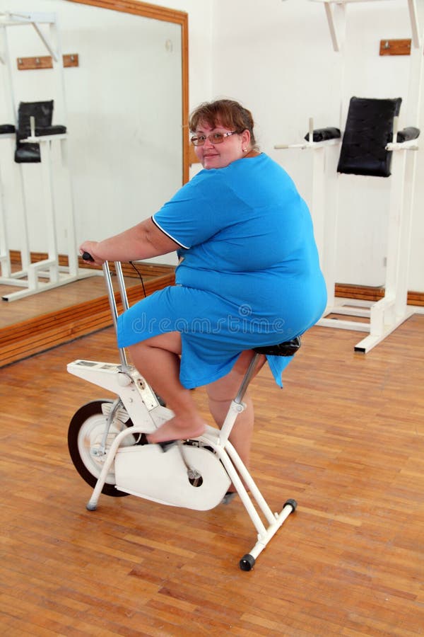Overweight woman exercising on bike. Simulator stock photos