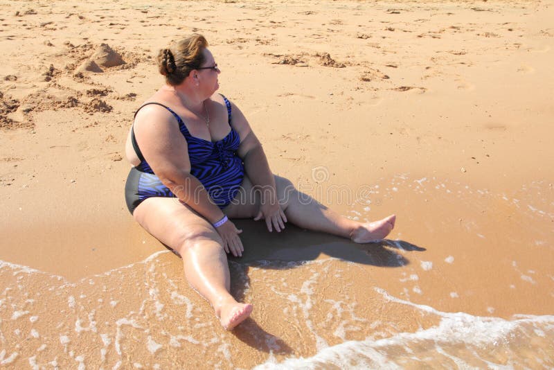 Overweight woman sitting on beach stock images
