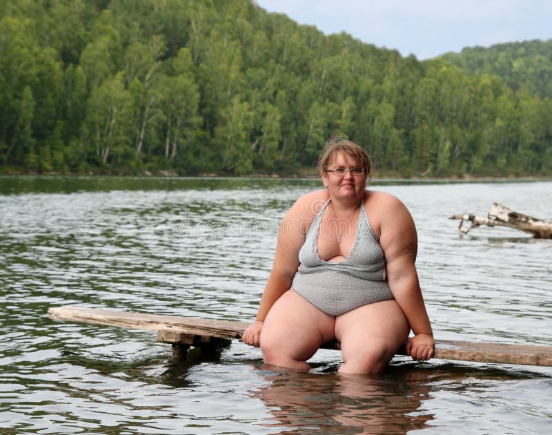 Sovrappeso donna seduta sul palco in un lago.