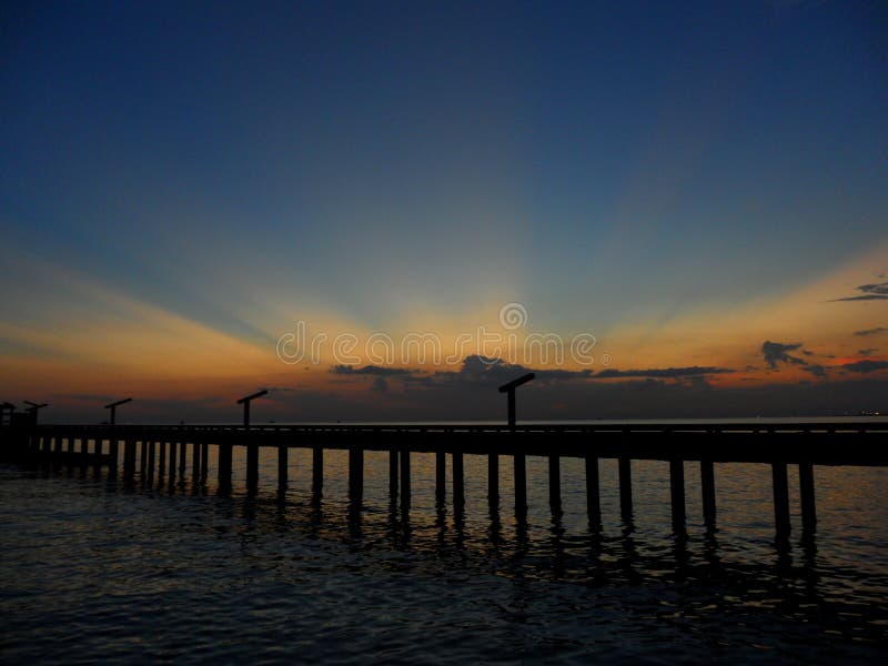 Overweldigen oranjegeel na gloed op donkerblauwe zonsonderganghemel over de brug aan het overzees stock afbeelding Overweldigen oranjegeel na gloed op donkerblauwe zonsonderganghemel over de brug aan het overzees stock afbeelding