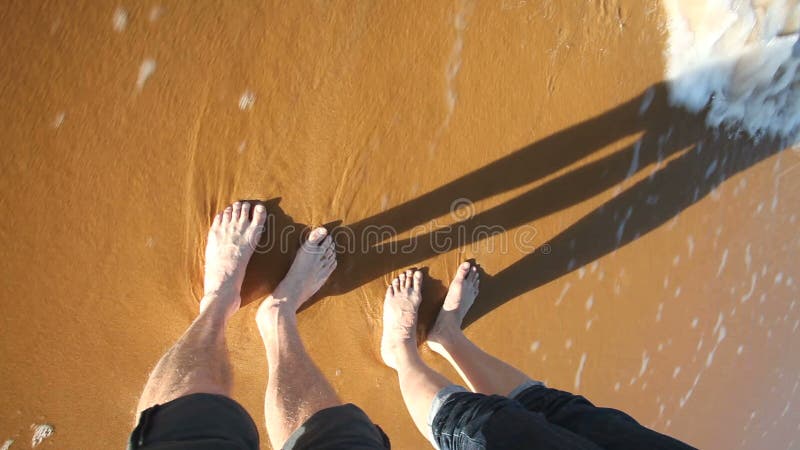 Overzeese golven die vrouw en man benen op zandig strand bespatten