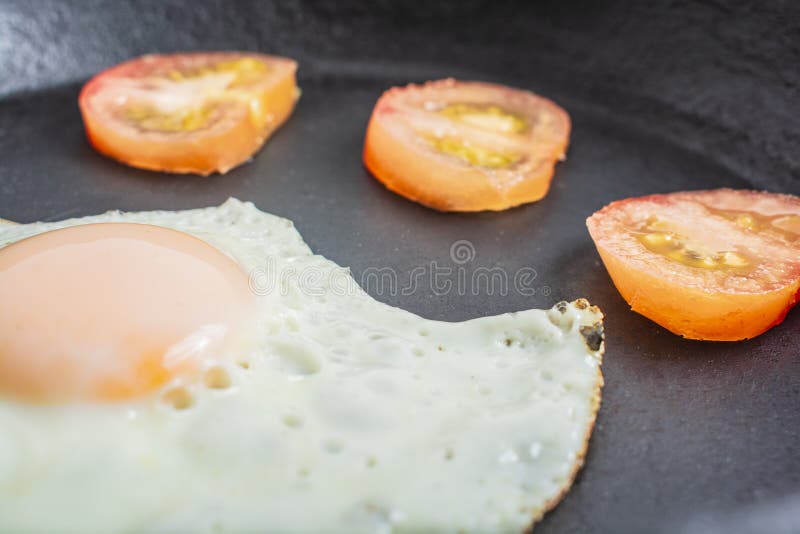 Ovo frito com tomates em uma frigideira do ferro fundido em uma tabela de madeira imagem de stock Ovo frito com tomates em uma frigideira do ferro fundido em uma tabela de madeira imagem de stock