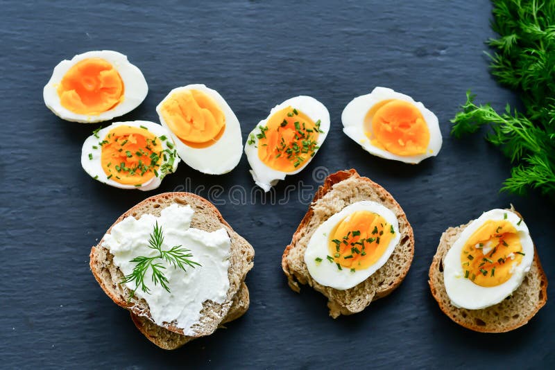 Bio Fresh hard boiled eggs sliced and broken with onion on black background .Sandwiches with soft cream cheese and whole grain bread . Bio Fresh hard boiled eggs sliced and broken with onion on black background .Sandwiches with soft cream cheese and whole grain bread .