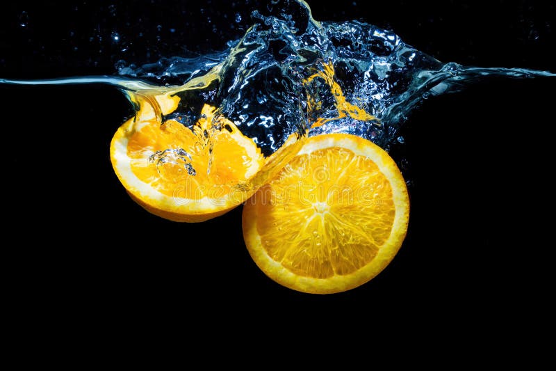 Juicy orange fruit halves dipped into the water with splashes on black. Juicy orange fruit halves dipped into the water with splashes on black