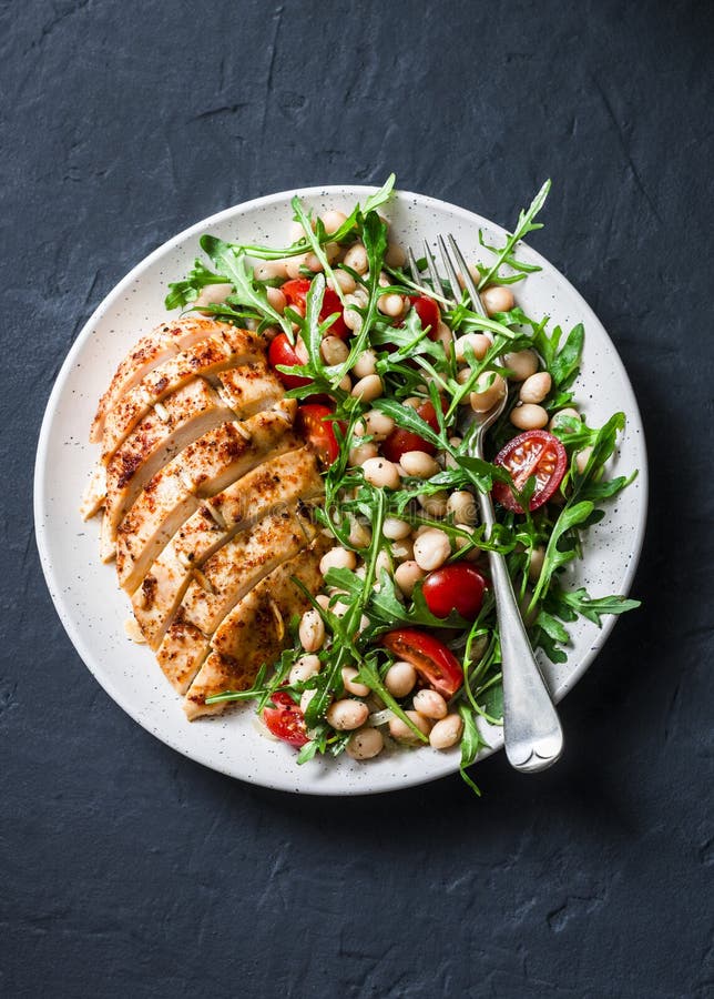 Очень вкусный здоровый обед - испеченные куриная грудка и белые фасоли, arugula, салат томатов вишни на темной предпосылке стоковое изображение rf Очень вкусный здоровый обед - испеченные куриная грудка и белые фасоли, arugula, салат томатов вишни на темной предпосылке стоковое изображение rf