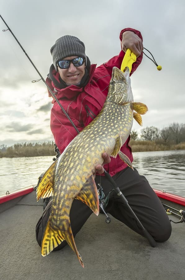 Happy fisherman with big pike fish trophy at the boat with fishing tackles. Happy fisherman with big pike fish trophy at the boat with fishing tackles.