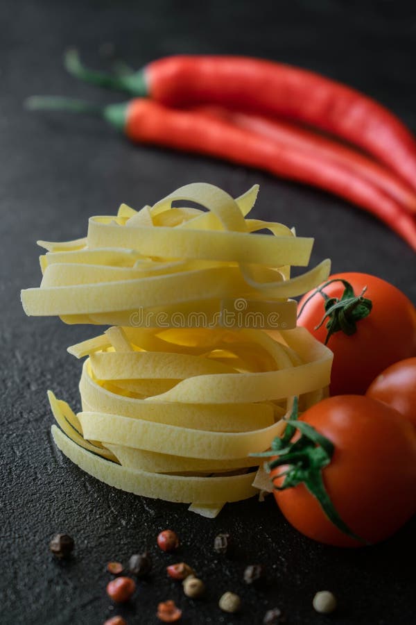 P?tes crues de fettuccine avec la tomate fra?che, les grains de poivre noirs et les poivrons de piment photographie stock P?tes crues de fettuccine avec la tomate fra?che, les grains de poivre noirs et les poivrons de piment photographie stock