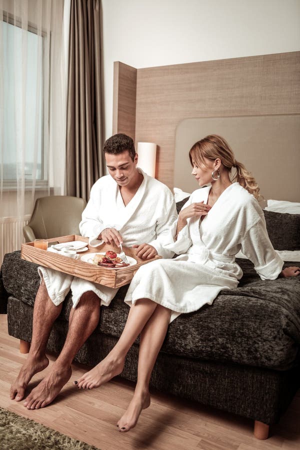 Paar dat hotelbadjassen draagt die op hotelbed zitten stock foto Paar dat hotelbadjassen draagt die op hotelbed zitten stock foto