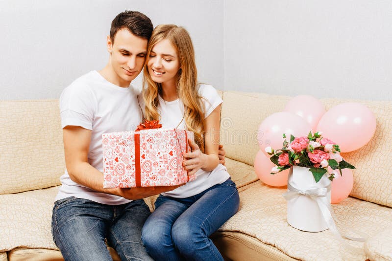 Paar in der Liebe, Mann gibt ein Geschenk, Frau sitzt zu Hause auf dem Sofa, Konzept des Tages der Frauen lizenzfreies stockfoto Paar in der Liebe, Mann gibt ein Geschenk, Frau sitzt zu Hause auf dem Sofa, Konzept des Tages der Frauen lizenzfreies stockfoto