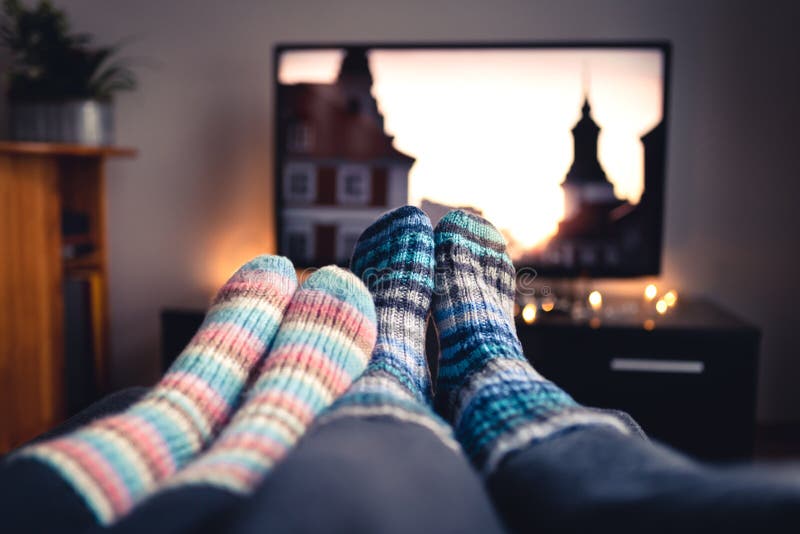 Paar die met sokken en wollen kousen op films of reeksen over TV in de winter letten Vrouw en man zitting of het liggen samen op