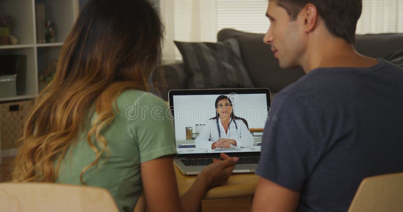 Paar die tussen verschillende rassen met arts op laptop spreken stock afbeeldingen Paar die tussen verschillende rassen met arts op laptop spreken stock afbeeldingen