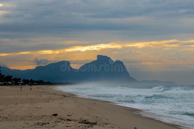 Paar en hond die op het strand van Barra da Tijuca in een mooie dageraad met de steen van Gavea op de achtergrond lopen - Rio de stock fotografie Paar en hond die op het strand van Barra da Tijuca in een mooie dageraad met de steen van Gavea op de achtergrond lopen - Rio de stock fotografie