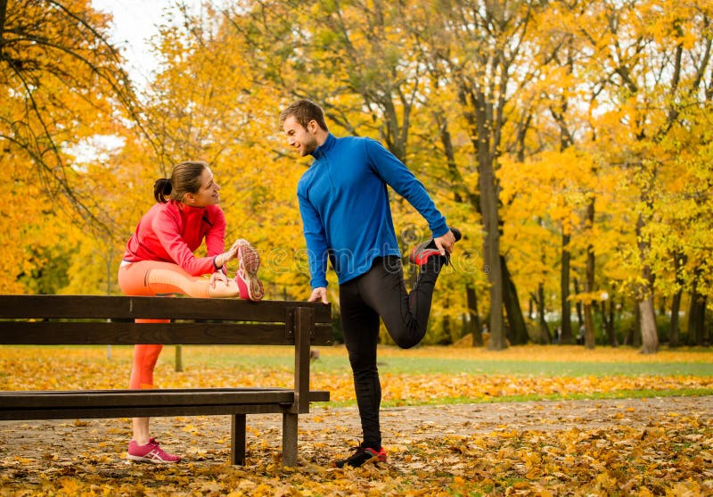 Young couple stretching muscles on bench before jogging in autumn nature. Young couple stretching muscles on bench before jogging in autumn nature