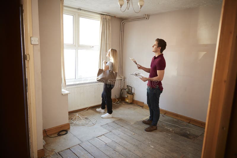 Couple Buying House For First Time Looking At House Survey In Room To Be Renovated. Couple Buying House For First Time Looking At House Survey In Room To Be Renovated