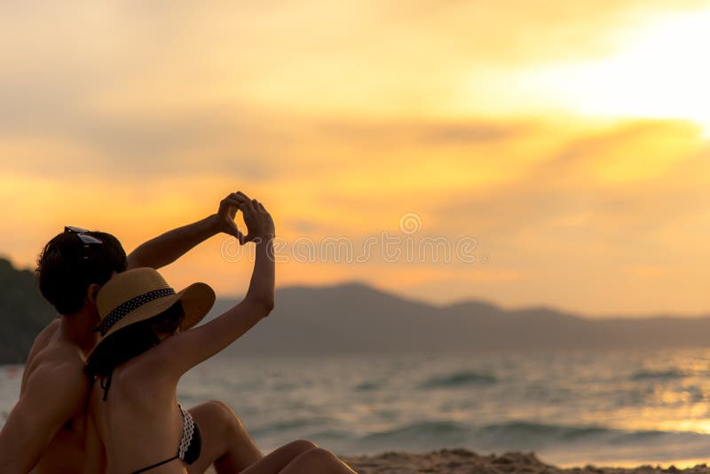 Paar in liefde die een hart maken - vorm met handen op tropisch op het zonsondergangstrand in vakantie royalty-vrije stock foto Paar in liefde die een hart maken - vorm met handen op tropisch op het zonsondergangstrand in vakantie royalty-vrije stock foto