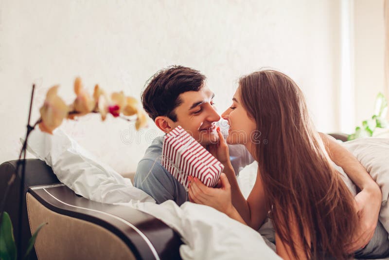 Paar in liefde kussen die in bed in de ochtend liggen De mens geeft giftdoos aan zijn meisje voor Valentijnskaartendag stock foto Paar in liefde kussen die in bed in de ochtend liggen De mens geeft giftdoos aan zijn meisje voor Valentijnskaartendag stock foto