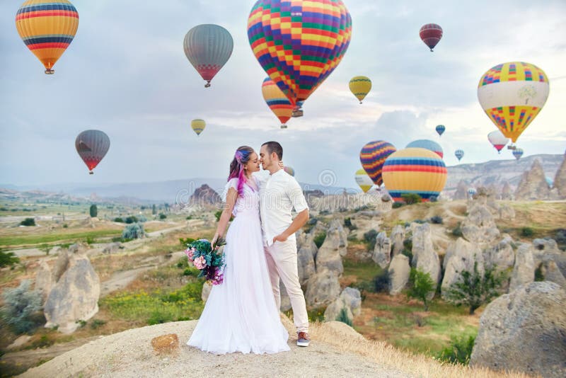 Paar in liefdetribunes op achtergrond van ballons in Cappadocia De man en een vrouw op heuvel bekijken een groot aantal vliegende royalty-vrije stock foto's Paar in liefdetribunes op achtergrond van ballons in Cappadocia De man en een vrouw op heuvel bekijken een groot aantal vliegende royalty-vrije stock foto's