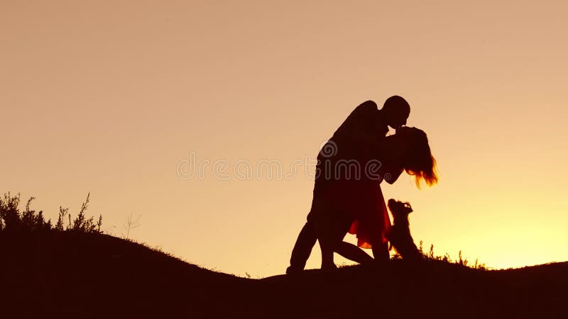 Paare in der Liebestanzen-Schattenbildnatur am Sonnenuntergang und am Küssen Liebevoller Mann und Frau mit Hundetanzen silhouetti