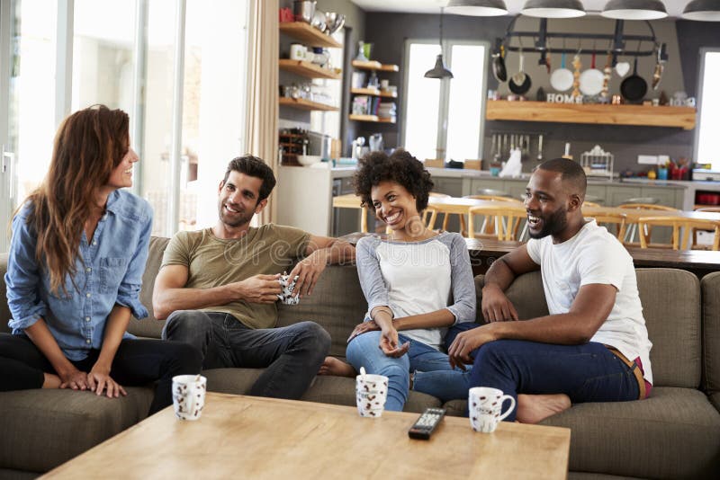 Couple Sitting On Sofa With Friends At Home Talking. Couple Sitting On Sofa With Friends At Home Talking