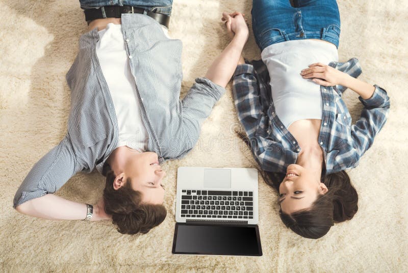 Paare, die auf Teppich zwischen Laptop liegen lizenzfreies stockbild Paare, die auf Teppich zwischen Laptop liegen lizenzfreies stockbild