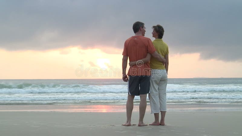 Paare, die den Sonnenaufgang auf einem Strand erwägen