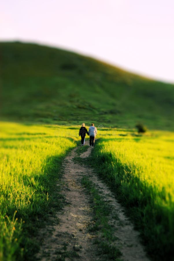 A couple holding hands while walking down a road in a green meadow. A couple holding hands while walking down a road in a green meadow.