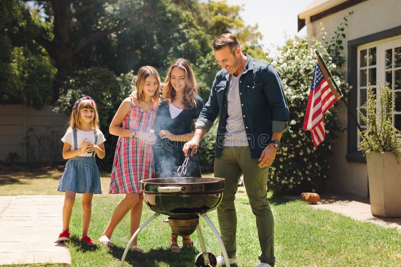 Paare, die mit ihren Kindern in ihrem Hinterhof macht barbequ stehen stockfotografie Paare, die mit ihren Kindern in ihrem Hinterhof macht barbequ stehen stockfotografie