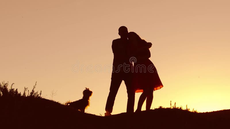 Paare im Liebestanzenschattenbild am Sonnenuntergang und am Küssen Liebevoller Mann und Frau mit Hundetanzen silhouettieren die l