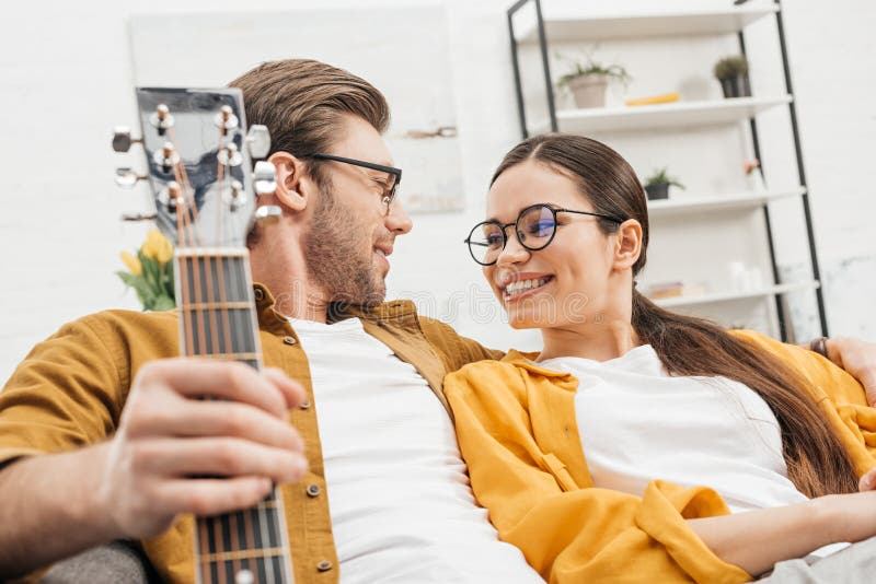 Paare mit der Gitarre, die auf Couch sitzt stockfotografie