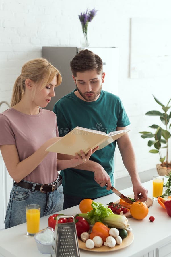 Paare von den strengen Vegetariern, die Nahrung mit Kochbuch zubereiten lizenzfreie stockfotografie Paare von den strengen Vegetariern, die Nahrung mit Kochbuch zubereiten lizenzfreie stockfotografie