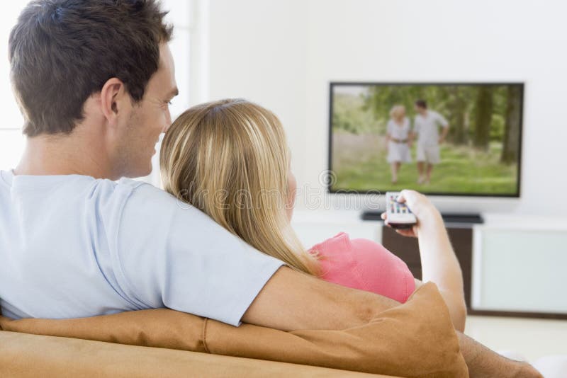 Paare in überwachendem Fernsehen des Wohnzimmers lizenzfreies stockbild