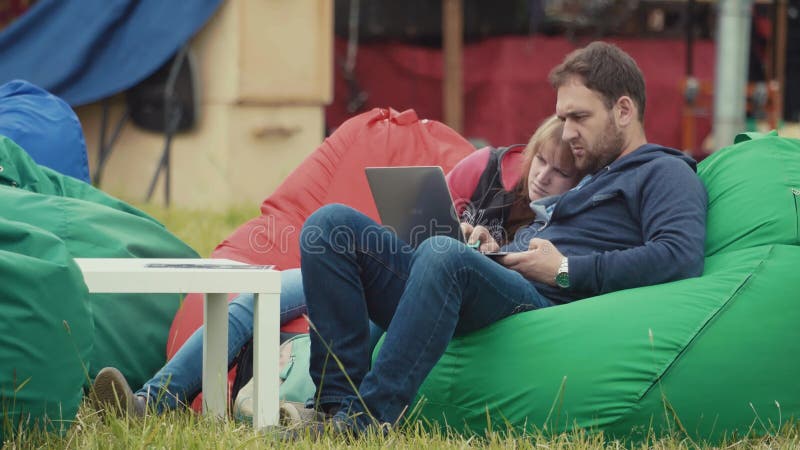 Paarzitting op kinderspelstoelen op grasgazon in stadspark met laptop