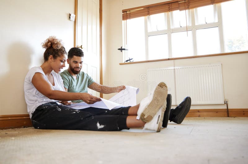 Paarzitting op Vloer die Plannen in Lege Zaal van Nieuw Huis bekijken royalty-vrije stock afbeelding Paarzitting op Vloer die Plannen in Lege Zaal van Nieuw Huis bekijken royalty-vrije stock afbeelding