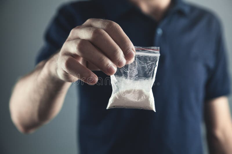 Pacchetto di plastica della tenuta del trafficante di droga con la polvere della cocaina immagini stock Pacchetto di plastica della tenuta del trafficante di droga con la polvere della cocaina immagini stock