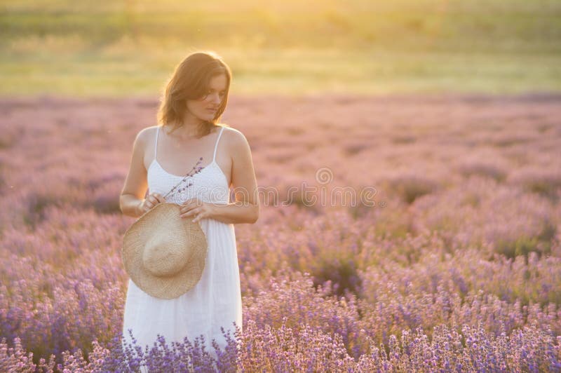 Beautiful young woman wearing a white dress standing in a moment of peace and serenity in a middle of a lavender field under the golden light of sunset. Beautiful young woman wearing a white dress standing in a moment of peace and serenity in a middle of a lavender field under the golden light of sunset.