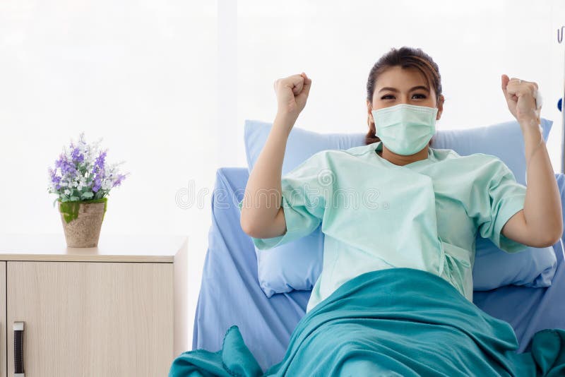 Paciente asiático de las mujeres que se sienta en cama y aumentos de hospital sus brazos La mujer joven recuperarse de enfermedad foto de archivo libre de regalías Paciente asiático de las mujeres que se sienta en cama y aumentos de hospital sus brazos La mujer joven recuperarse de enfermedad foto de archivo libre de regalías