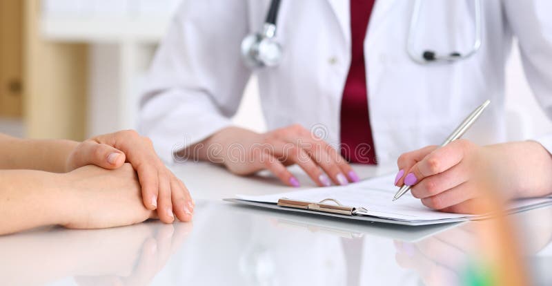 Paciente de consulta da mulher desconhecida do doutor ao encher-se acima de um formul?rio de candidatura na mesa no hospital Apen imagens de stock royalty free Paciente de consulta da mulher desconhecida do doutor ao encher-se acima de um formul?rio de candidatura na mesa no hospital Apen imagens de stock royalty free