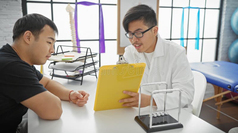Paciente de consulta de médicos asiáticos en clínica moderna con ropa de laboratorio y gafas que hablan de salud fotografía de archivo libre de regalías