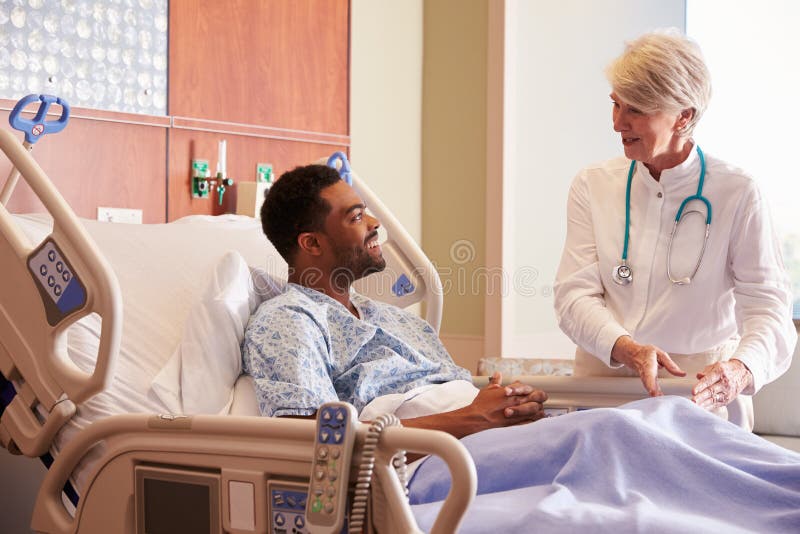 Paciente fêmea do doutor Talking To Male na cama de hospital imagem de stock royalty free Paciente fêmea do doutor Talking To Male na cama de hospital imagem de stock royalty free