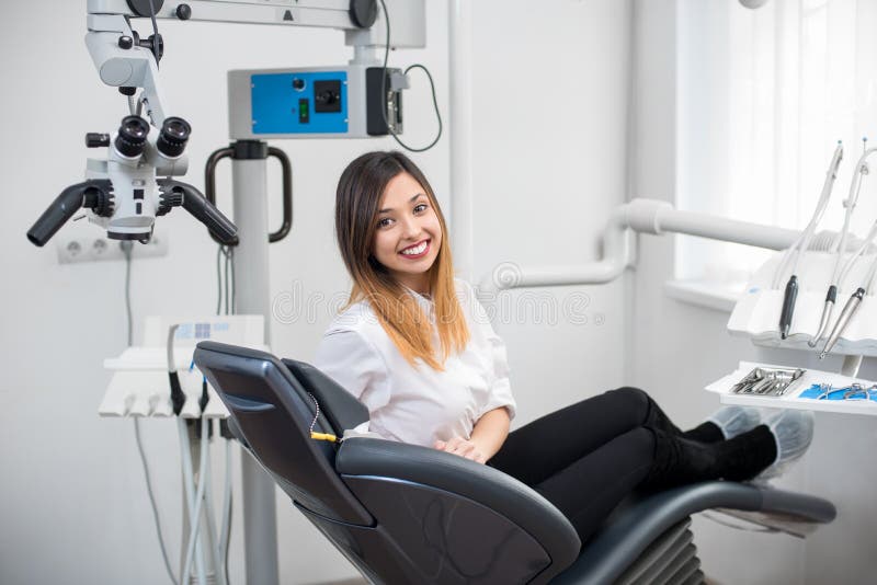 Paciente fêmea novo bonito com os dentes brancos perfeitos que sentam-se na cadeira dental e que sorriem após o tratamento foto de stock royalty free Paciente fêmea novo bonito com os dentes brancos perfeitos que sentam-se na cadeira dental e que sorriem após o tratamento foto de stock royalty free