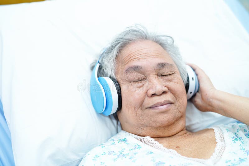 Paciente mayor o mayor asiático de la mujer de la señora mayor escuchar la música mientras que acuéstese en cama en sala de hospi foto de archivo Paciente mayor o mayor asiático de la mujer de la señora mayor escuchar la música mientras que acuéstese en cama en sala de hospi foto de archivo
