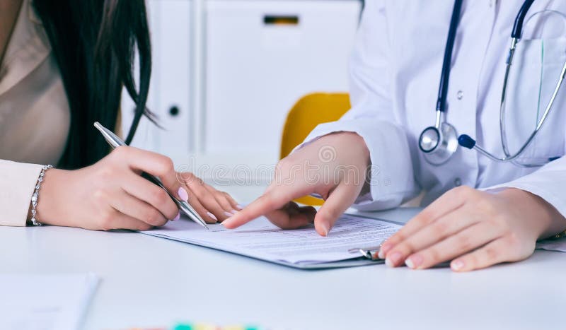 Paciente que firma el contrato médico El doctor de sexo femenino explica cómo rellenar el impreso médico fotografía de archivo Paciente que firma el contrato médico El doctor de sexo femenino explica cómo rellenar el impreso médico fotografía de archivo