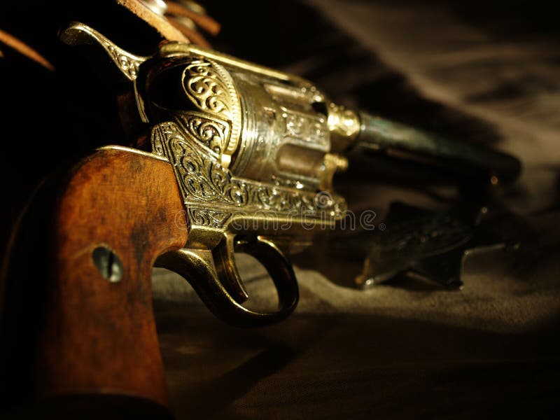 Detail photo of a Peacemaker resting on a leather holster with a badge in the background. Detail photo of a Peacemaker resting on a leather holster with a badge in the background