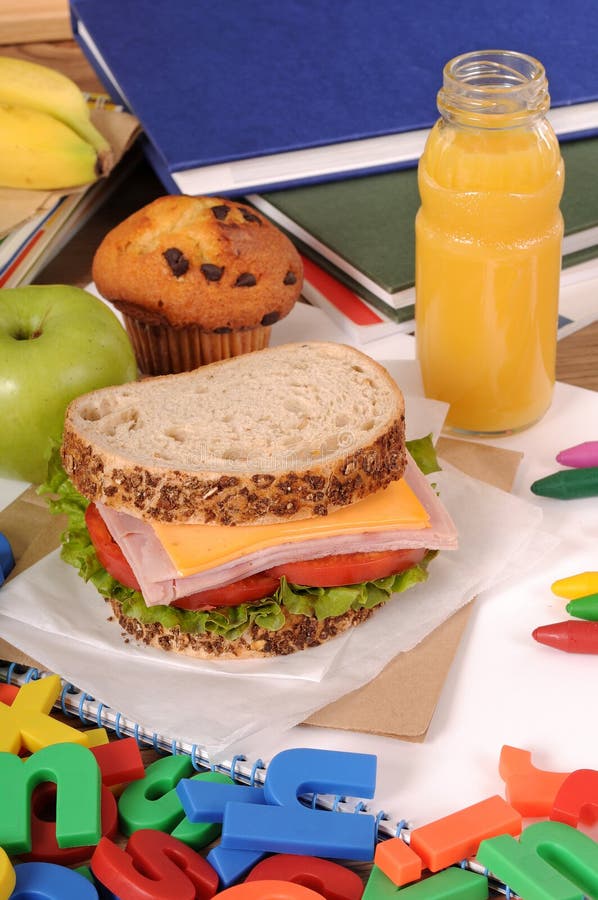 Packed school lunch: sandwich, cake, apple and drink on classroom desk stock photo Packed school lunch: sandwich, cake, apple and drink on classroom desk stock photo