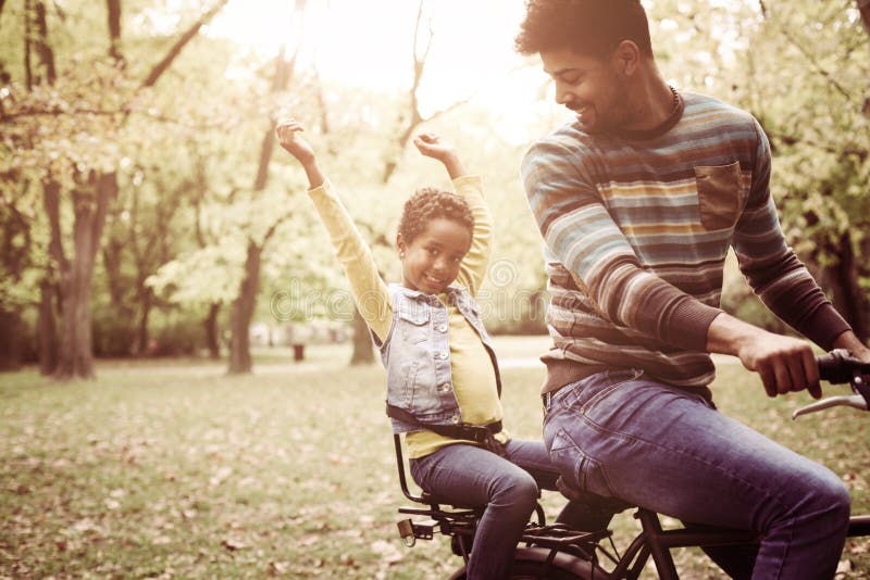 Padre afroamericano que conduce a su niña en la bici tr imagen de archivo libre de regalías Padre afroamericano que conduce a su niña en la bici tr imagen de archivo libre de regalías